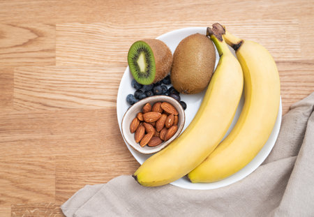A plate with fruit bananas, kiwi, blueberries and nuts on a wooden background. The concept of healthy eating. Dietary products. Top view,  free space for text.の写真素材