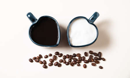 Two cups in the form of hearts with freshly brewed aromatic coffee with milk and espresso and scattered grains on yellow background. The concept of opposite drinks. Top view.の写真素材