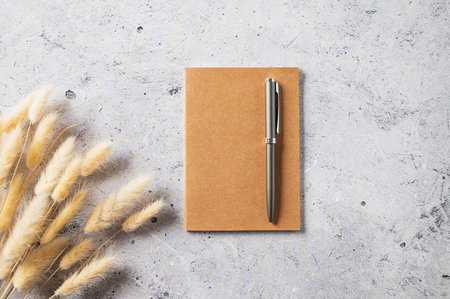 Home office workspace layout with a craft notebook, pen and dried bouquet on gray concrete background. Top view and copy space.の写真素材