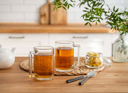 Two cups of tea with teapot and dry herbal flowers on a wooden countertop against the background of a white kitchen in the early morning. Healthy breakfast concept.の写真素材