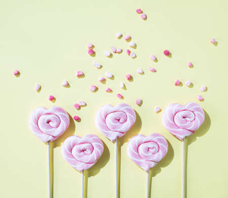 Pink lollipops in the shape of hearts with color sugar on a yellow background. Top view and copy space.の写真素材