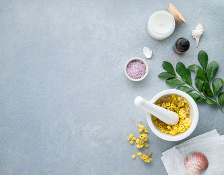 Organic dry flowers for the body and facial massager with sea salt, creme, candle and towel on a blue background. Skin care. The concept of a natural spa product. Top view and copy space.の写真素材