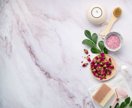 flat lay with organic sea salt with dried rose flowers, soap, candle, brush and gua sha on a pink marble background. The concept of a natural spa product. Top view and copy space.の写真素材