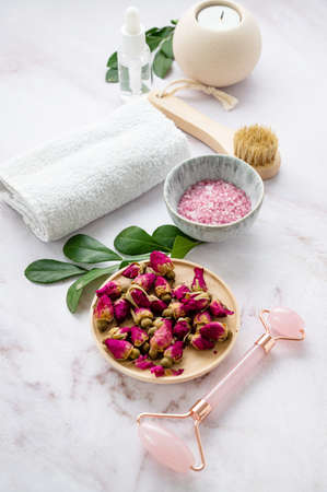 Organic sea salt for the body with dried rose flowers, candle, brush, towel and gua sha on a pink marble background. The concept of a natural spa product. Skin care.の写真素材