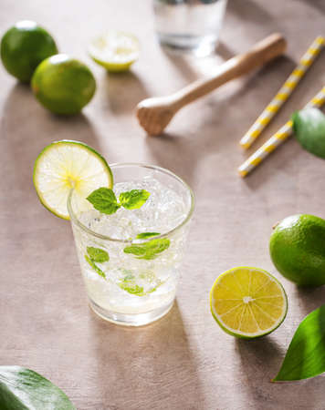 Refreshing mojito cocktail with mint and lime in a glass with ice on pink background with morning shadows. Concept summer citrus drink.の写真素材