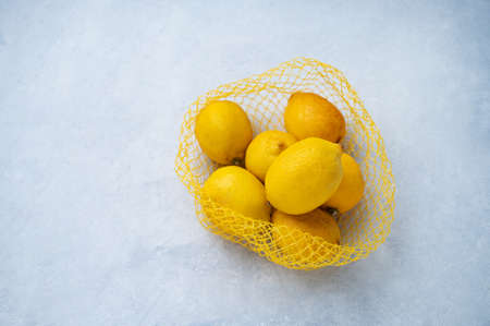 Fresh yellow lemons in a plastic bag on a  blue texture background. The concept of healthy eating. Top view and copy space.の写真素材