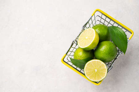 Fresh limes in a supermarket basket on a light textured background. Citrus fruit concept for freshly squeezed lime mojito. Copy space and top view.の写真素材
