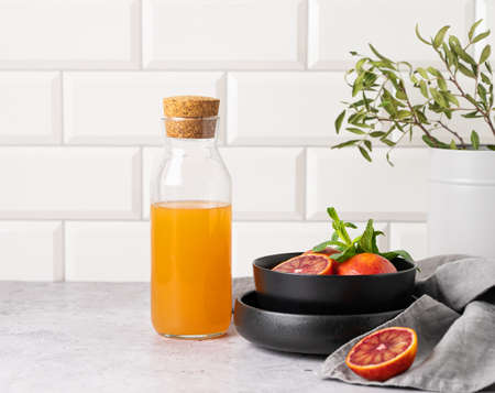 Freshly squeezed orange juice in a bottle on the kitchen table with fresh red oranges on plate. The concept of a healthy drink. Front view and copy  space.の写真素材
