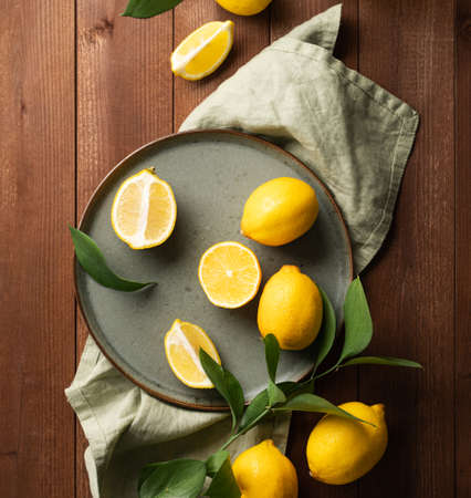 Fresh lemons with leaves in a green plate on a dark wooden background. Citrus fruits for freshly squeezed lemonade. Dark composition and rustic style. Top view.の写真素材