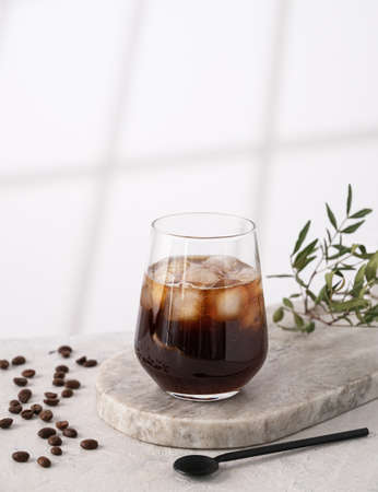 Iced coffee in a glass with ice cubes and grains on a light marble background with morning shadows. The concept of a cold summer drink. Copy space.の写真素材