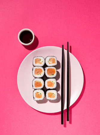 Japanese Sushi roll with salmon, cucumber and soy sauce with chopsticks in the plate on pink background with hard shadow. Concept food photography. Top view and copy space.の写真素材