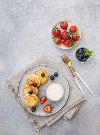 Cheesecakes or cottage cheese with fresh blerries and sour cream on a gray background. The concept of healthy and delicious breakfast. Top view and copy space.の写真素材
