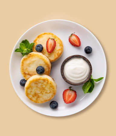Cottage cheese pancakes with sour cream, mint, blueberries and strawberries  on a yellow background. Healthy and delicious breakfast. Top view.の写真素材