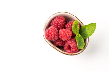 Juicy forest raspberry with mint leaf i a bowl on a white isolated background. Healthy food concept....