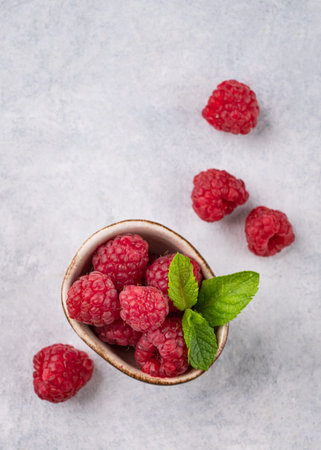Juicy forest raspberry with mint leaf i a bowl on a light textured background. Healthy food concept....