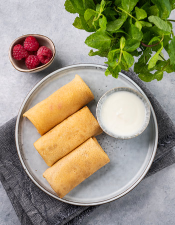 Homemade crepes with raspberry and sour cream on a plate on a light background with fresh mint close up. Healthy food concept. Top view.の写真素材