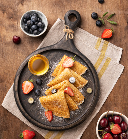 Homemade crepes with fresh berries and honey on a dark wooden plate on a brown background. Healthy food concept. Top view.の写真素材