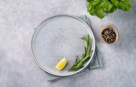 An empty plate on a blue background with a slice of lemon, rosemary, spices and fresh basil. The concept of healthy food. Top view and copy space.の写真素材