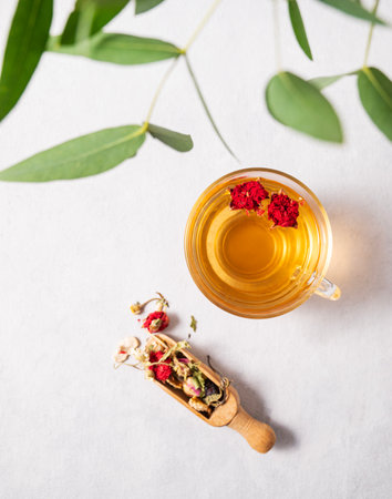 Fragrant herbal tea with pomegranate flowers in a glass cup on a white background with eucalyptus branches. The concept of a healthy drink for breakfast. Top view and space for text.の写真素材