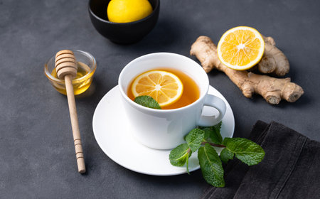 Cup of tea with lemon, honey and mint on a dark background. The concept of a healthy drink for immunity with ginger and herbs. Diet and antioxidant tea.の写真素材