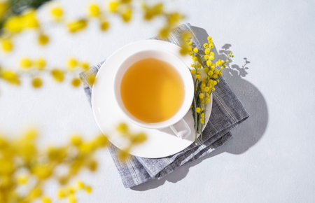 A spring bouquet with yellow mimosa flowers over a cup of herbal tea on a white table. Concept of 8 March, happy women's day. Top view and copy space.の写真素材