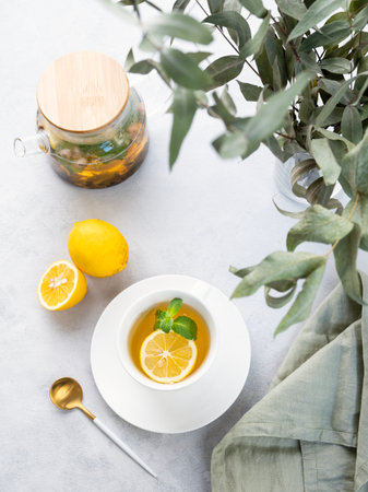 Herbal tea with lemon and mint in a white cup on a wooden plate on a light background with eucalyptus branches and a teapot. The concept of a healthy and delicious drink for   immunity. Top view.の写真素材