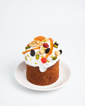 A cake with candied fruits and icing on a white plate on a white isolated background. The concept of...