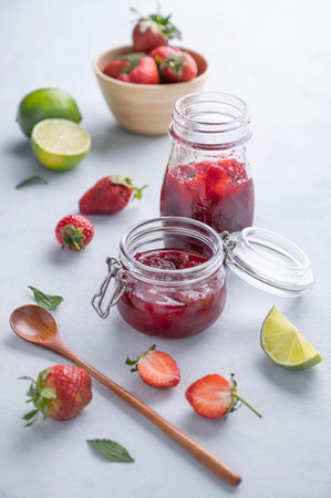 Homemade strawberry jam. Preserved food in a glass jar with fresh organic berries on a light background with lime. Eco-friendly farm products.の写真素材