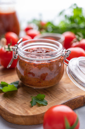 Homemade tomato sauce for pizza or pasta in a jar on a light background with fresh vegetables and herbs close up. The concept of classic Italian cuisine.の写真素材