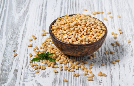Peeled cedar nuts in a wooden cup on a white wooden background. Rustic style. The concept of vegetarian and diet snacks. Free space for text.の写真素材