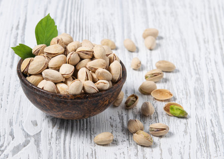 Nuts pistachio in a wooden cup on a white wooden background. Rustic style. The concept of vegetarian and diet snacks. Free space for text.の写真素材
