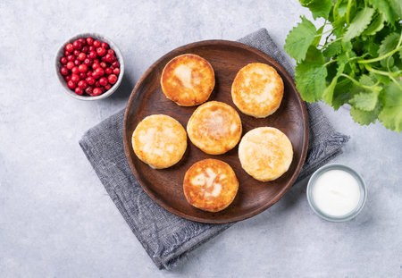 Pancakes with cottage cheese with fresh blerries and sour cream on a wooden plate on a blue background. The concept of a healthy and delicious morning breakfast. Top view and copy space.の写真素材