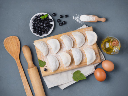 Dumplings with black currant. Delicious vegetarian vareniki with berries in a bowl on a gray background with herbs. Top view and copy space.の写真素材
