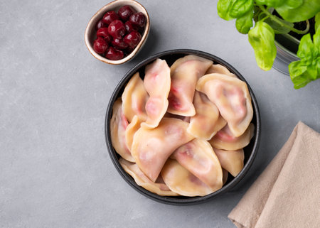 Dumplings with cherry. Delicious vegetarian vareniki with berries in a bowl on a gray background with herbs. Top view and copy space.の写真素材