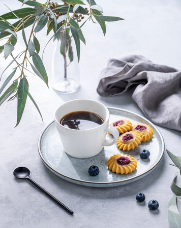 Black coffee espresso in a cup with homemade berry cookies and blueberries on a light background with eucalyptus branches. Concept spring morning breakfast.の写真素材