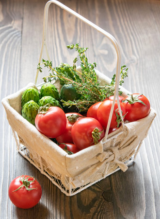 Fresh farm vegetables. Tomatoes, cucumbers and greens in a basket on a dark wooden background. The concept of healthy vegetarian food from the market.の写真素材