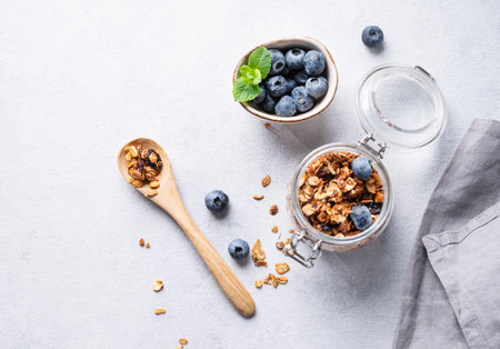 Homemade baked granola with nuts and fresh blueberry in a jar on a light background with napkin. Healthy vegetarian muesli for breakfast. Top view and copy space.の写真素材