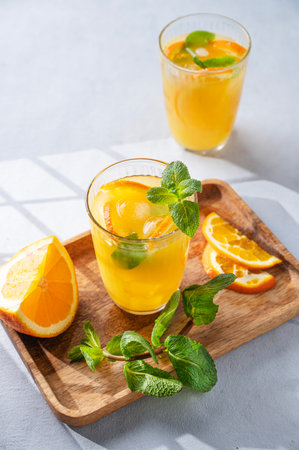 Orange juice with fresh fruits, mint and ice on a light background with shadow. Healthy freshly squeezed citrus detox drink for breakfast. Free space for text.の写真素材