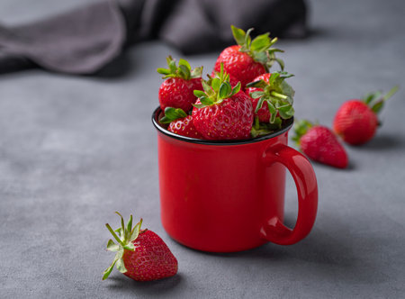 Juicy strawberries in a red cup on a dark background with napkin. Farm ripe healthy berries close up. Free space for text.の写真素材