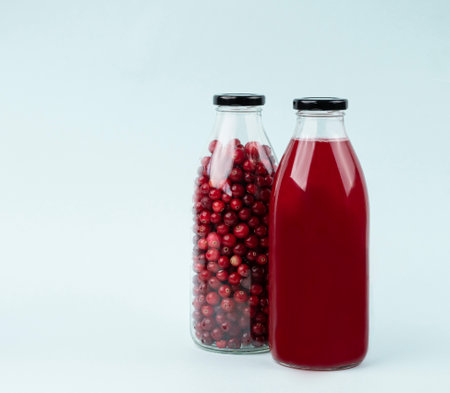 Bottle with berry juice from forest cranberries and lingonberries on a blue isolated background. Healthy drink concept. Front view.の写真素材