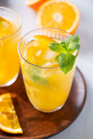 Freshly squeezed juice in a glass with fresh oranges, mint and ice on a light background close up. Healthy citrus detox drink for breakfast.の写真素材