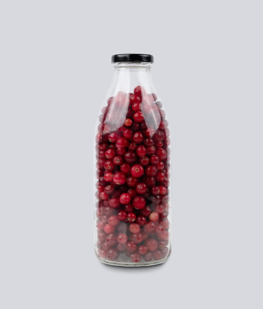 Bottle with wild cranberries and lingonberries on a gray isolated background. Healthy drink concept....
