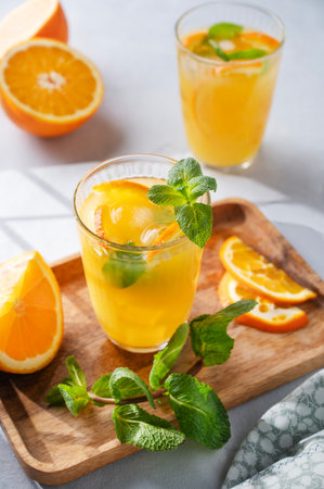 Freshly squeezed juice in a glass with fresh oranges, mint and ice on a light background with metallic tube and shadow. Healthy citrus detox drink for breakfast.の写真素材