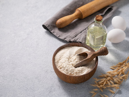 Oatmeal in a wooden bowl with a scoop, eggs and rolling pin on a blue background. Natural organic flour for home baking. Free space for text.の写真素材
