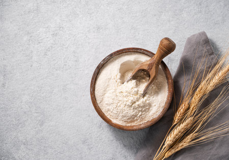 Natural wheat flour in a wooden bowl on a blue background with branches of wheat. The concept of an organic product for home baking. Top view and copy space.の写真素材
