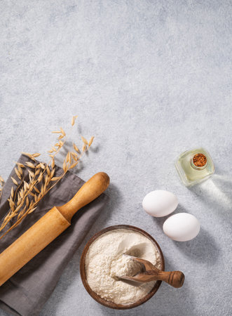 Oatmeal in a wooden bowl with eggs, oli and rolling pin on a blue background. Natural organic flour for home baking. Top view and copy space.の写真素材
