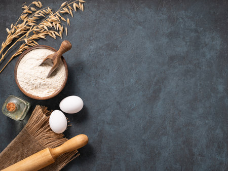 Oatmeal in a wooden bowl with eggs, rolling pin and oli on a dark blue background. Natural organic flour for home baking. Top view and copy space.の写真素材