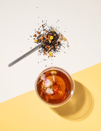 Creative flat lay of a glass cup of herbal tea with rose flowers on a yellow and white background with hard shadow. Food and drink concept. Top view and copy space.の写真素材