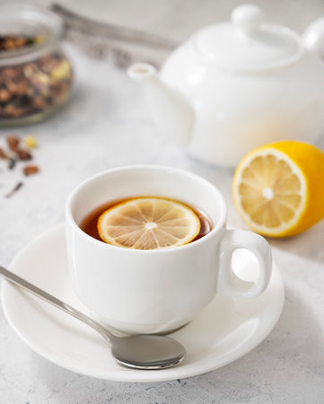Tea with lemon in a white cup on a light background with  a teapot close up. The concept of a healthy and tasty breakfast for immunity.の写真素材