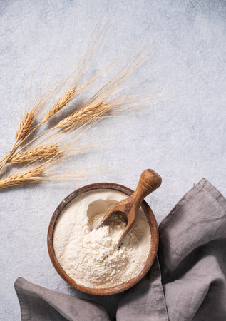 Natural wheat flour in a wooden bowl on a blue background with branches of wheat. The concept of an organic product for home baking. Top view and copy space.の写真素材